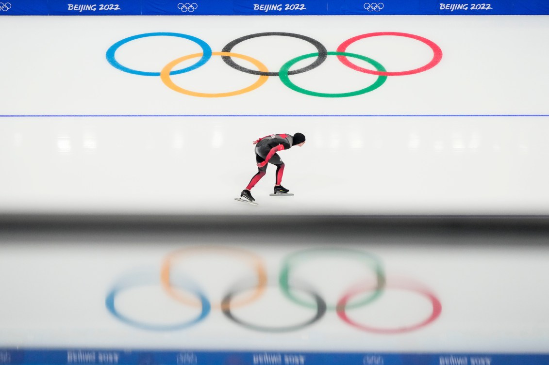 Wide shot of Graeme Fish with the Olympic rings reflected on the ice