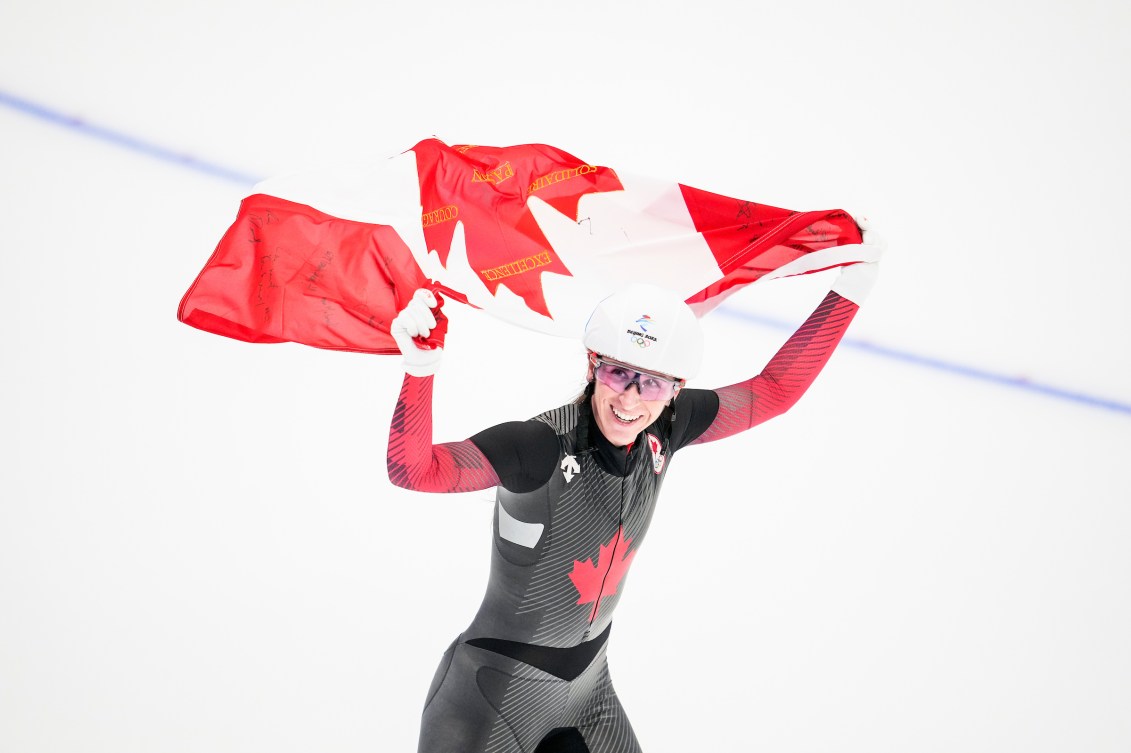 Ivanie Blondin holds the Canadian flag above her head on a victory lap 