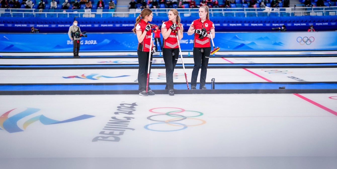 Three curlers stand by the side of an ice sheet