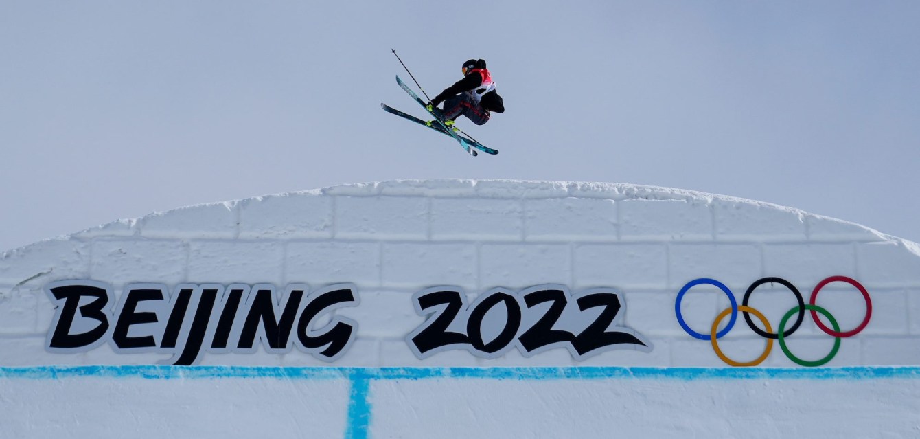 Max Mofftt performs a ski trick over a giant Beijing 2022 sign on the snow