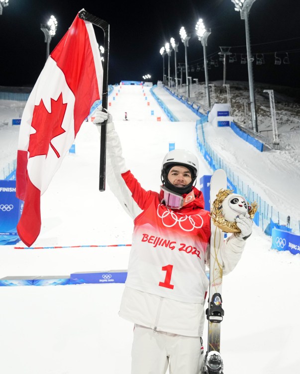 Mikael Kingsbury holds the Canadian flag on a hockey stick on the podium