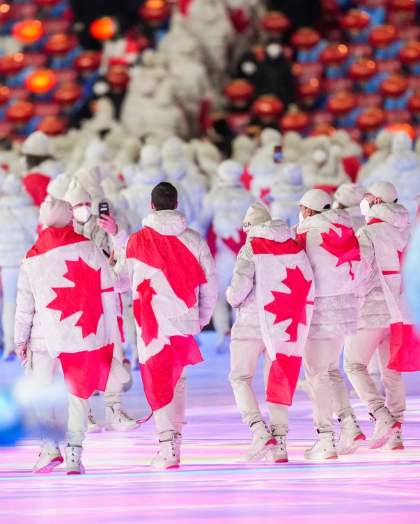 Backs of Team Canada athletes with Canadian flag draped 