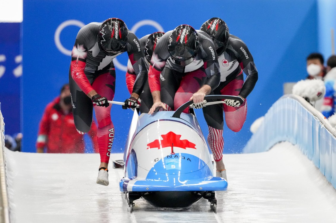 Front angle of four bobsledders running and pushing a bobsled