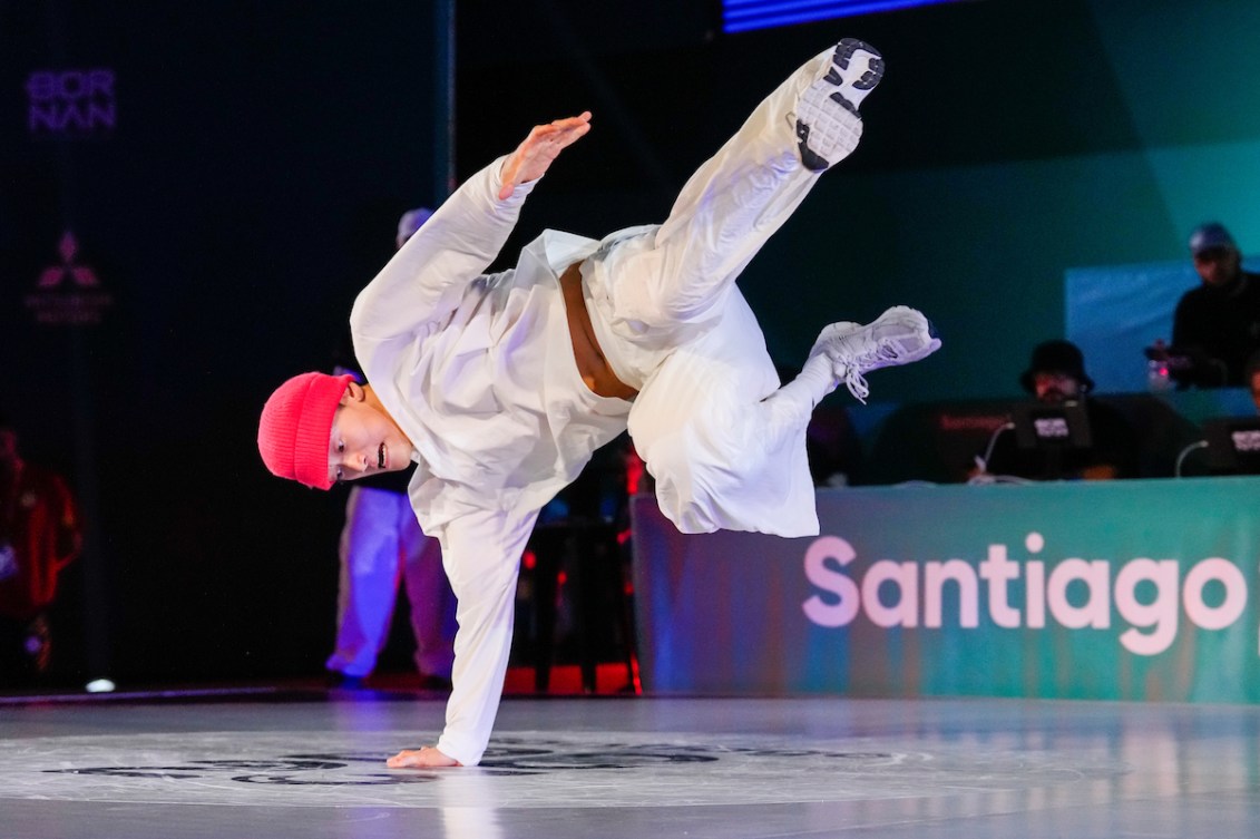 Phil Wizard in a white outfit and pink hat performs a dance move on one hand