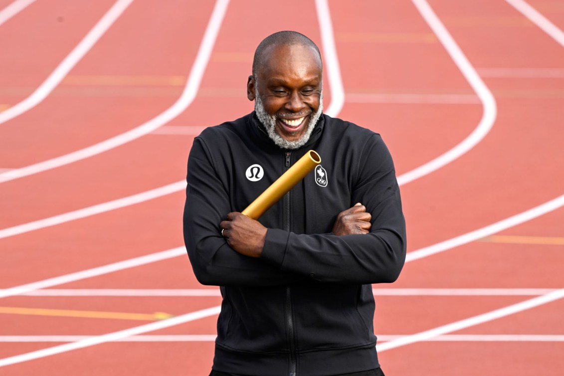 Bruny Surin holds a gold baton with his arms crossed on a running track 