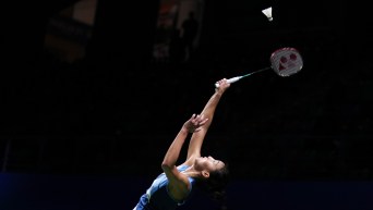 Michelle Li about to hit the shuttlecock with her racket in a darkened arena