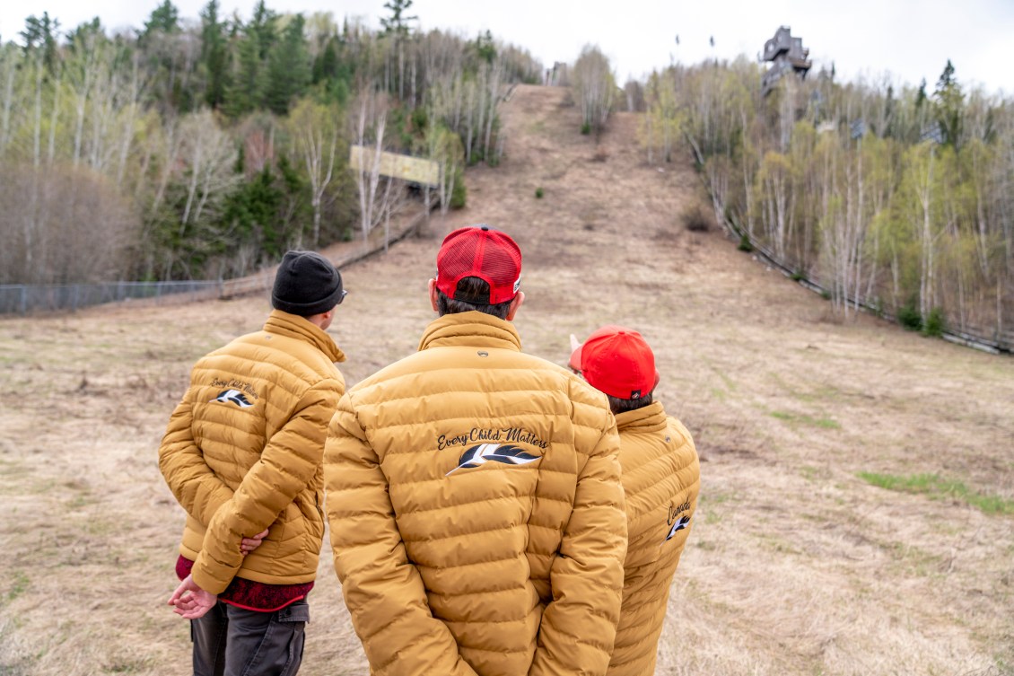 Three people stand back to camera as they look at the overgrown ski jumps at Big Thunder 