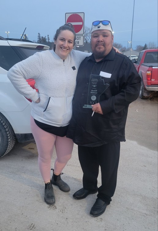 Two people pose for the camera while one holds an award