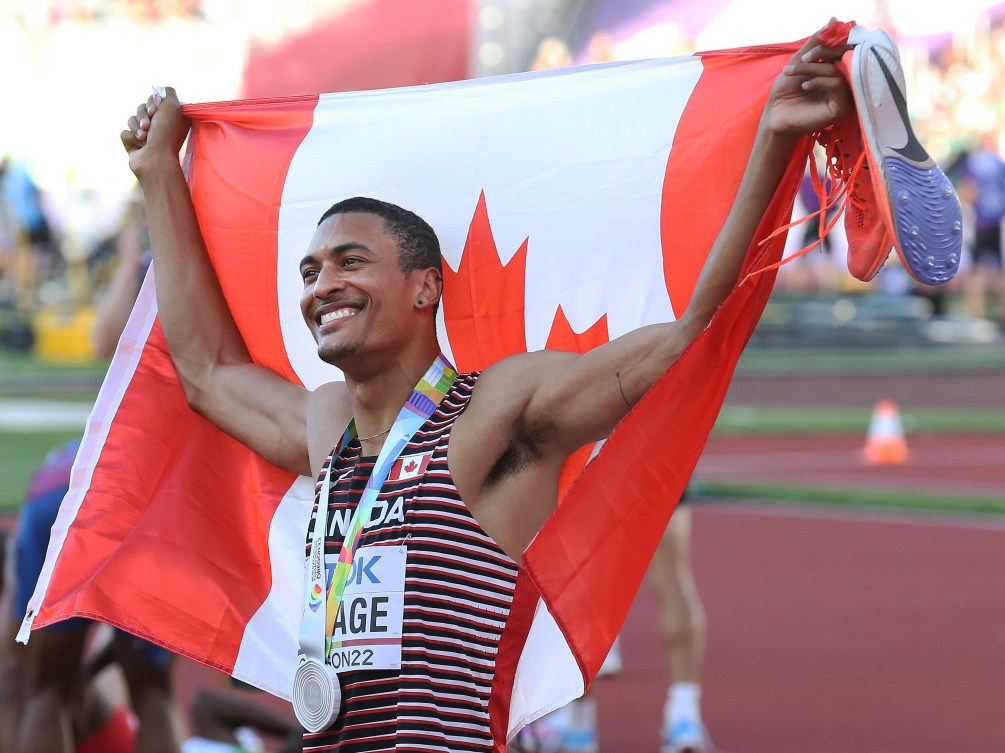 Pierce LePage wears his silver medal and holds the Canadian flag up behind him 