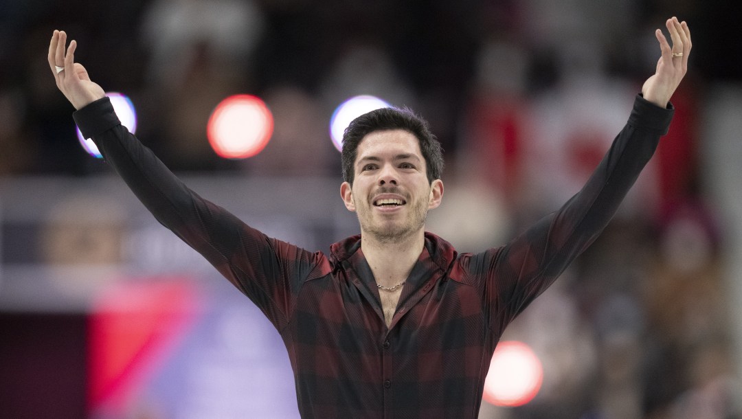 Keegan Messing in a plaid shirt raises his arms while smiling at the end of his performance