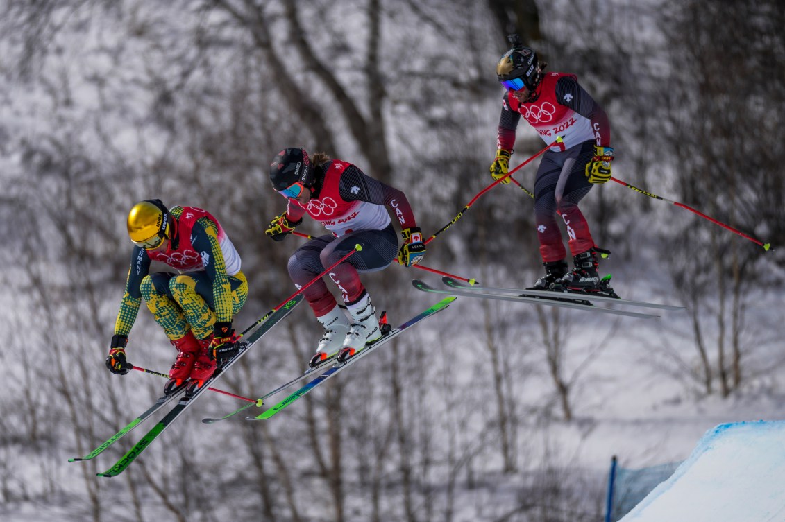 Three ski cross racers fly over a jump 