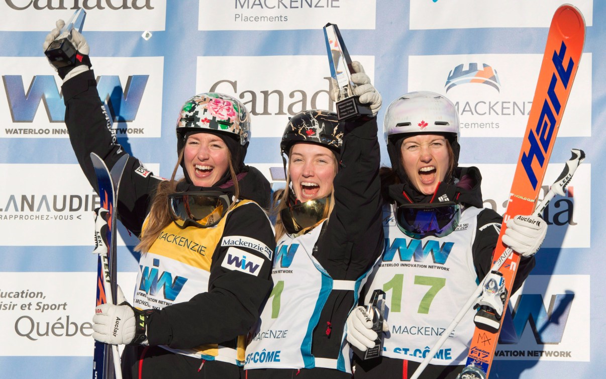 Three Dufour-Lapointe sisters smile and yell with joy on a podium 