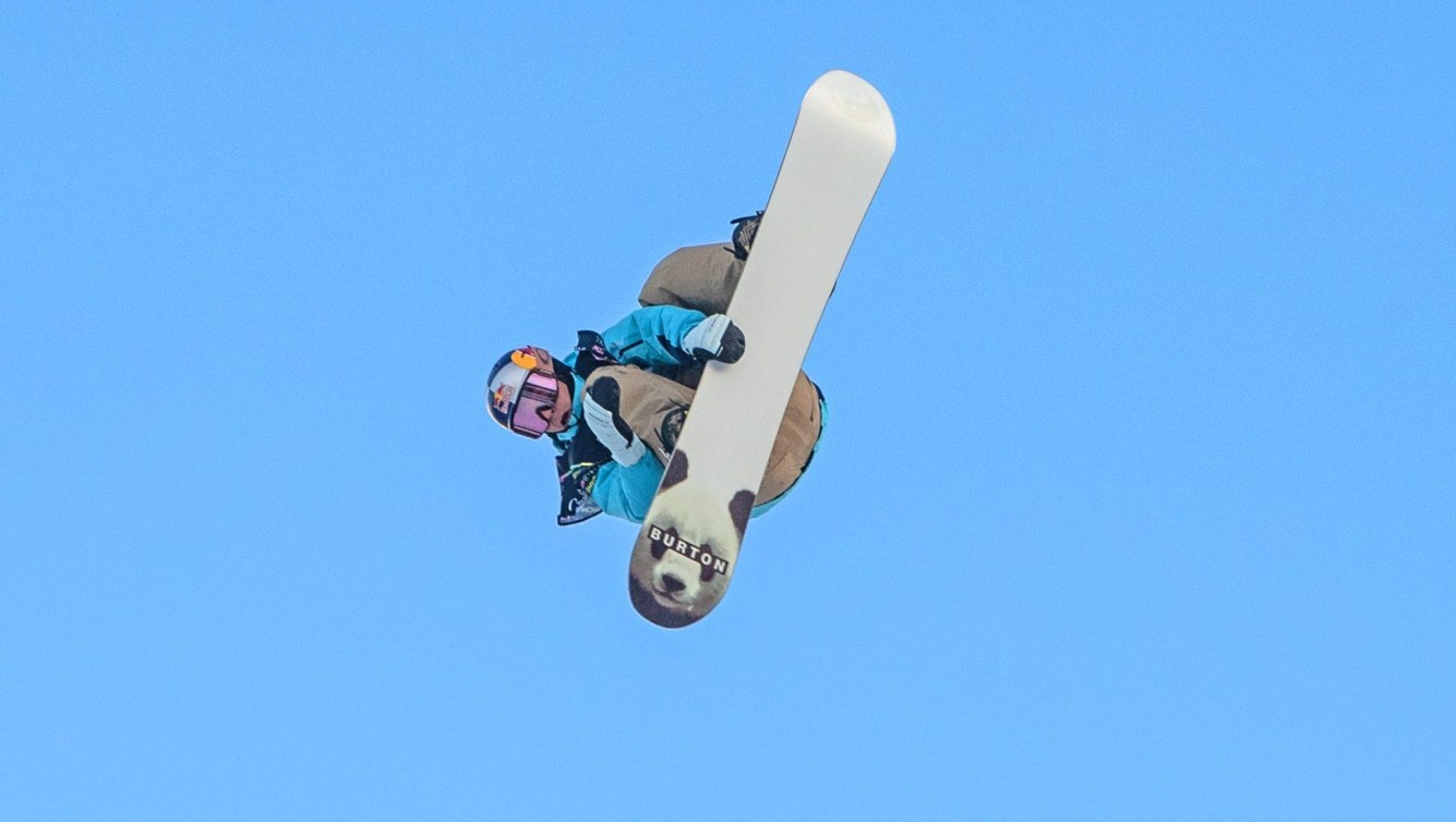 Mark McMorris grabs his snowboard while performing a trick against blue sky