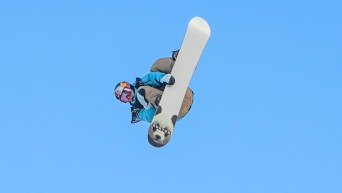 Mark McMorris grabs his snowboard while performing a trick against blue sky