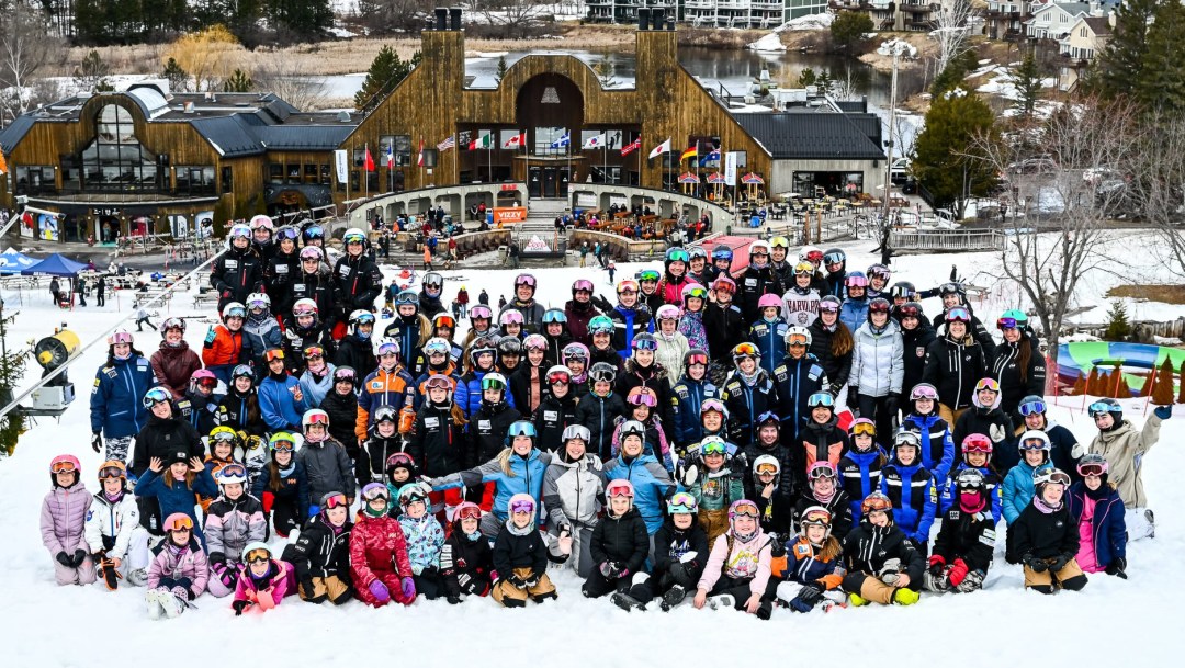A large group of young female skiers cheer in front of a chalet