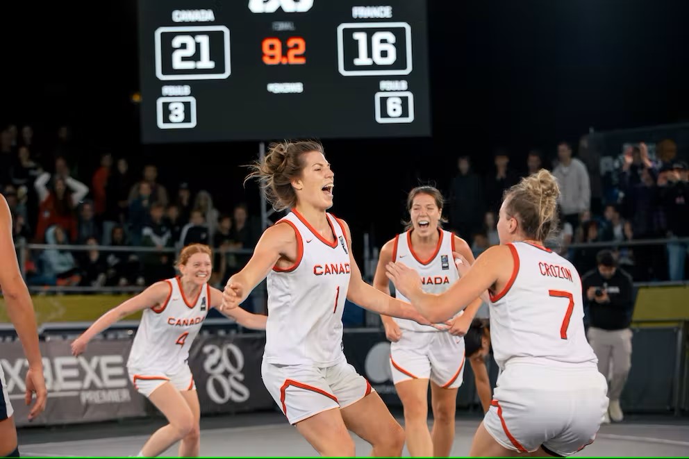 Four female basketball players in white about to jump and hug each other in celebration 