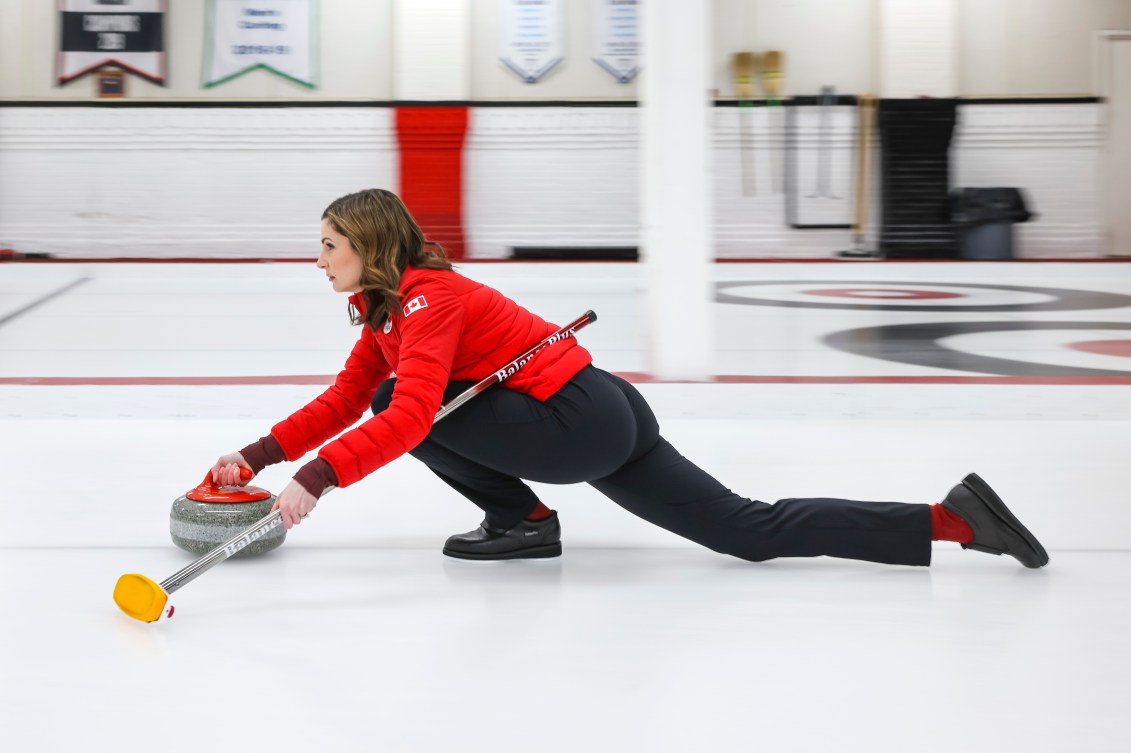 Side angle of Lisa Weagle throwing a curling stone while sliding on the ice 