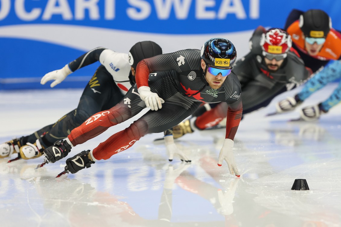 A group of short track speed skaters race around a turn 