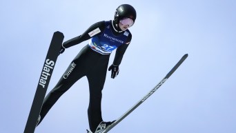 Ski jumper in all black flies against blue sky with skis in V shape