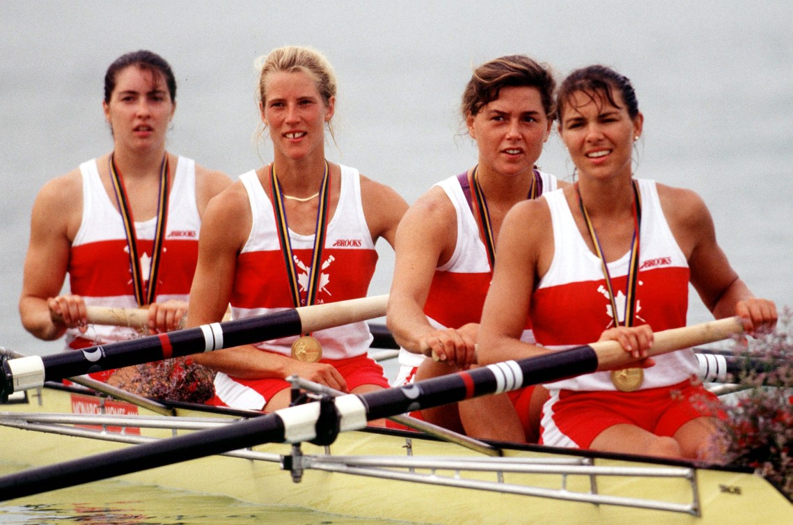 Four female Canadian rowers wear gold medals while sitting in their shell 
