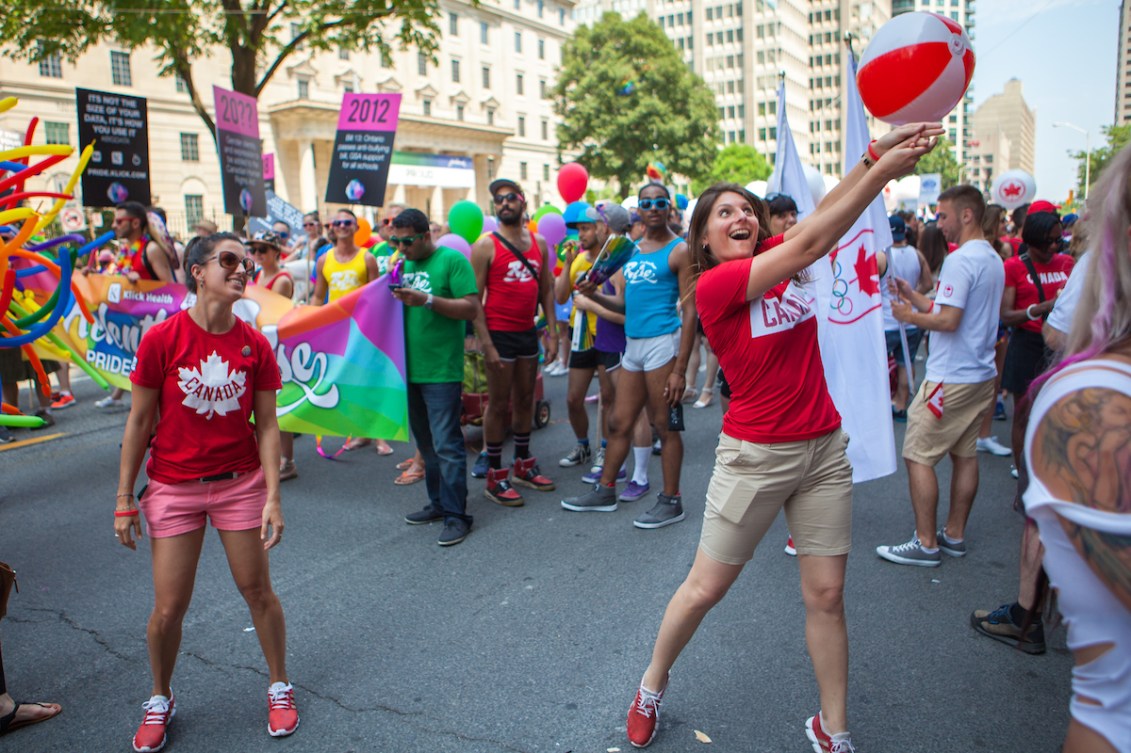 Two Canadian athletes laugh with a group marching in a pride parade