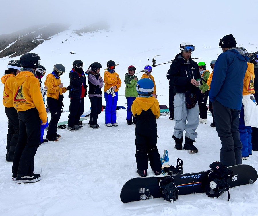 A group of young Indigenous snowboarders stand in a circle as part of a land acknowledgement and blessing