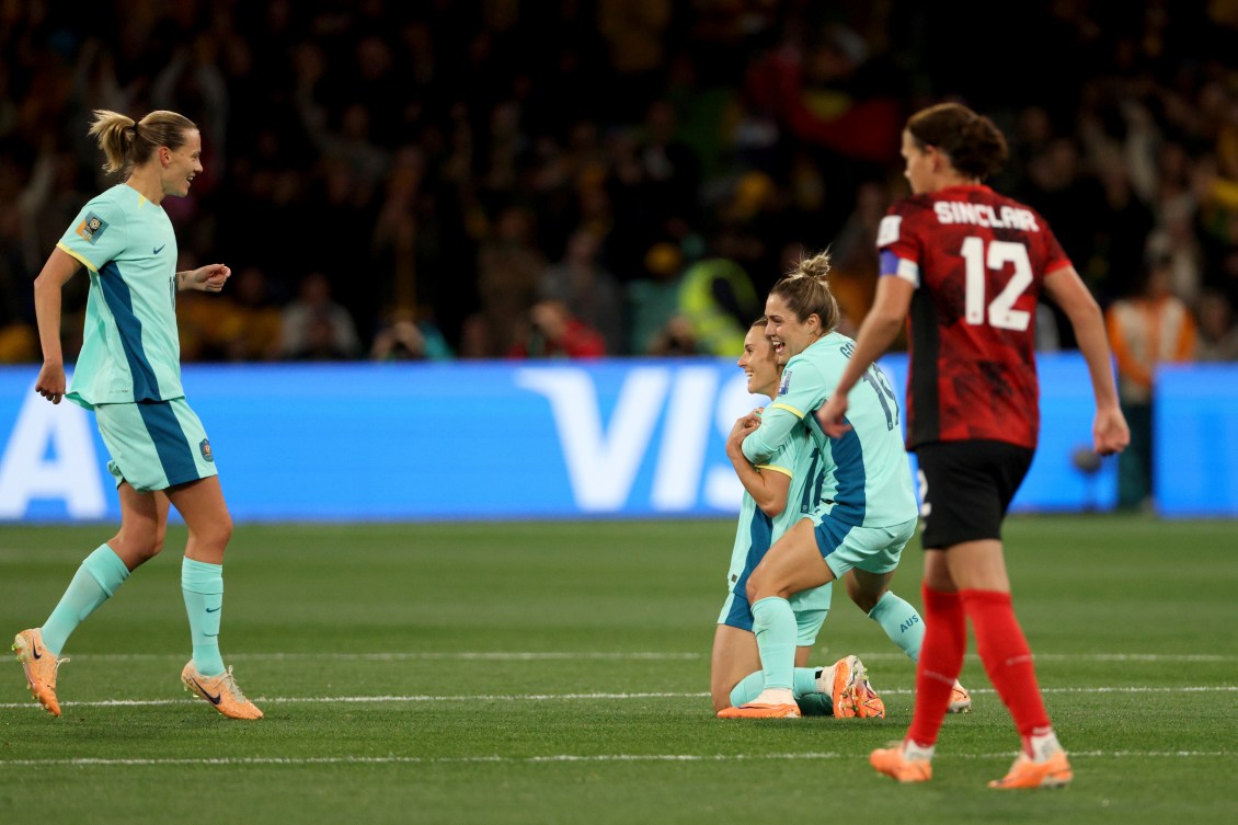 Australia players celebrate as Christine Sinclair looks on.