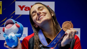 Pamela Ware smiles as she holds up her medal and stuffed mascot