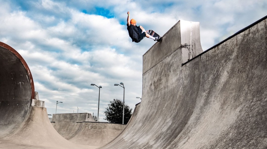 A skateboarder at the top of a concrete ramp in a skate park