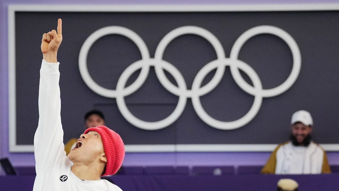 Phil Wizard celebrates by pointing up at the sky in front of the Olympic rings