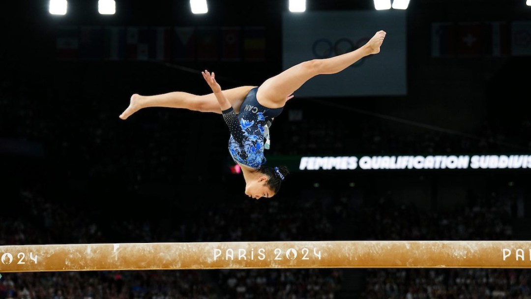 Aurelie Tran flips while on the balance beam, wearing a sparkly blue leotard