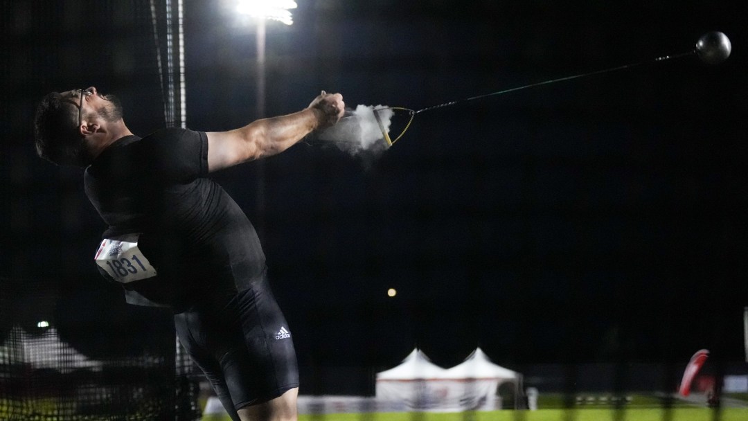 Adam Keenan dressed in black releases his hammer throw into the dark night