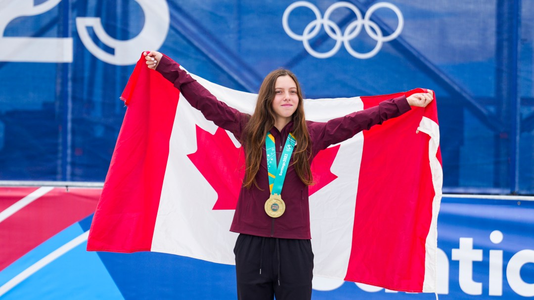 Athlete in burgundy jacket poses with her gold medal and a Canadian flag