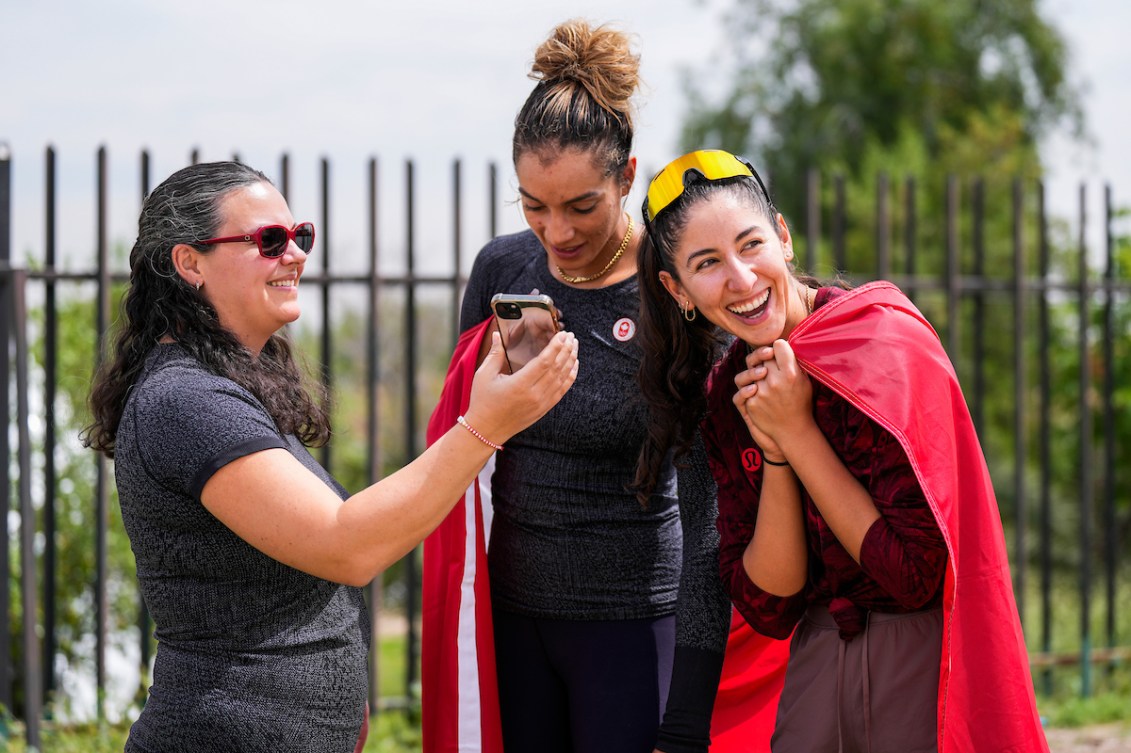 Melissa Humana-Paredes and Brandie Wilkerson smile while looking at something on a cell phone 