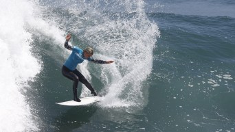 Sanoa Demple-Olin in a teal top and black wetsuit surfs a wave