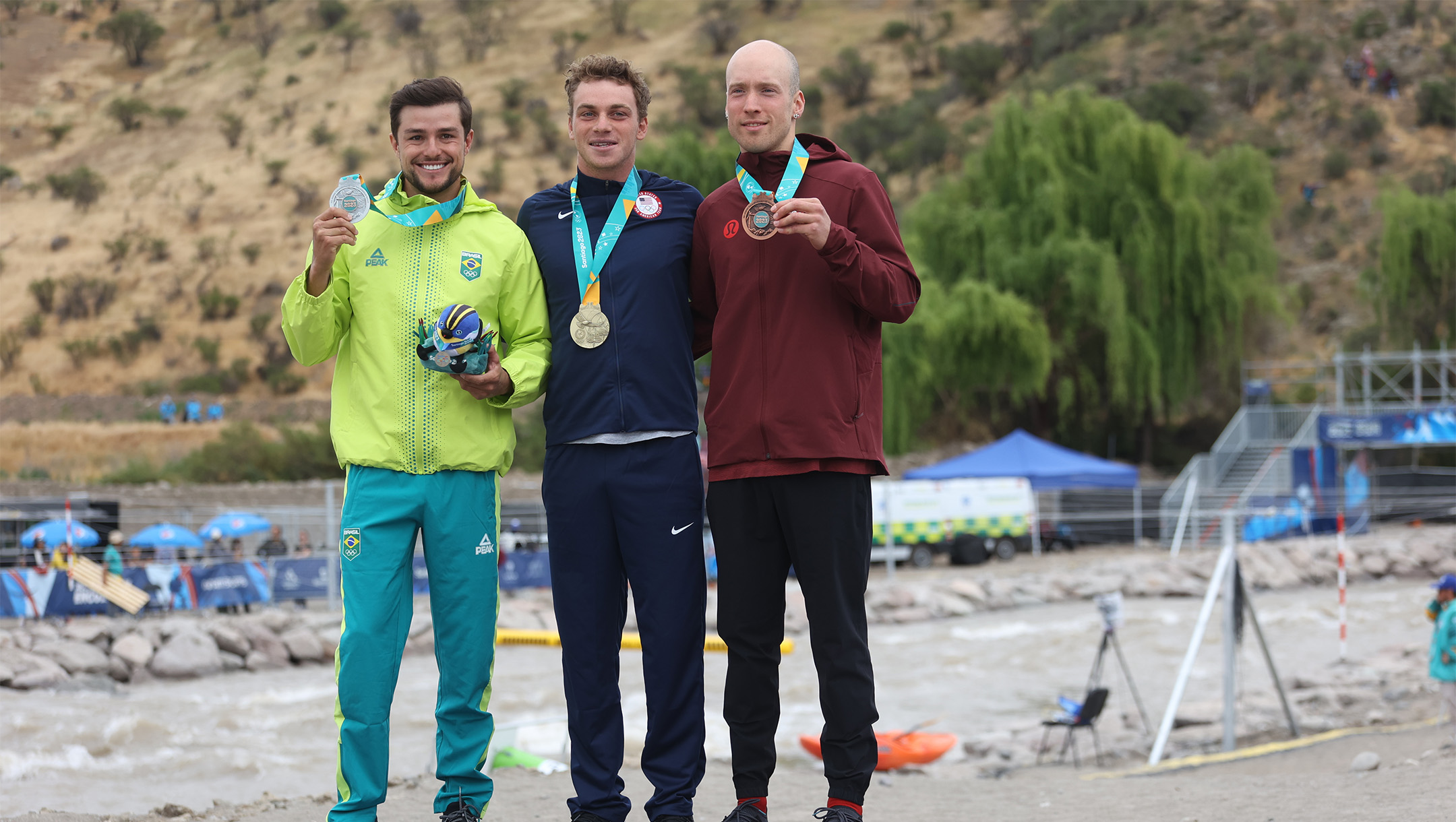 Three male athletes, including one in Team Canada attire stand on the podium.