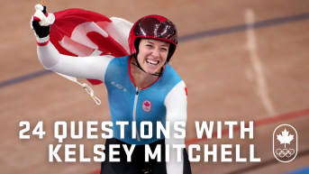 Woman finishes competing and cheers on bike while holding a Canada flag.