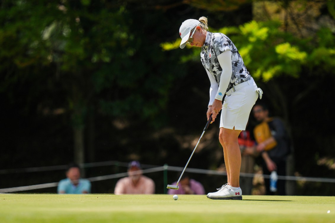 A female golfer for Team Canada wears all white and takes a put.