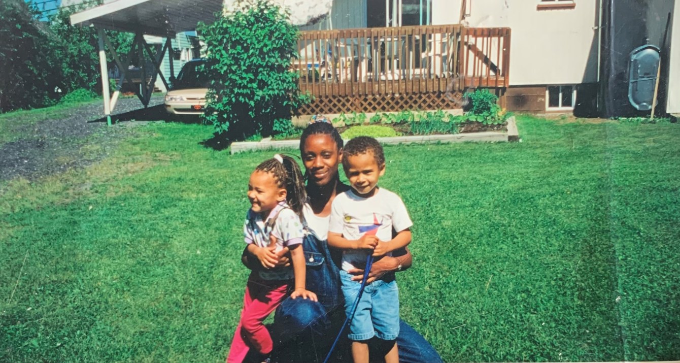 A mom and two kids hug each other on a green lawn.