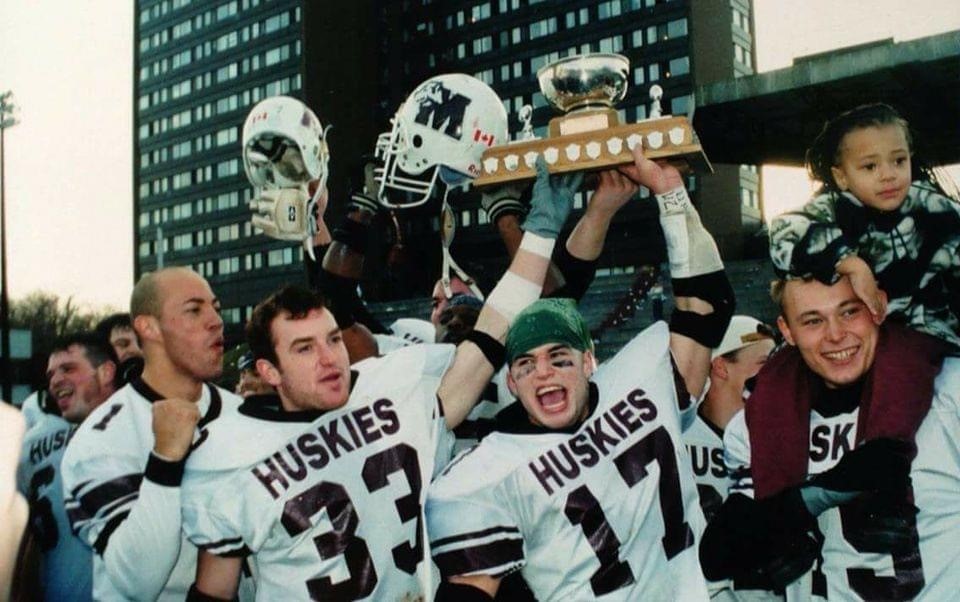 A group of football players hold up a trophy while a little girl sits on the shoulders of one player