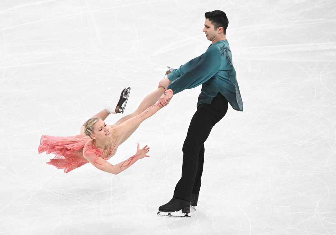 Zachary Lagha in a green shirt and black pants swings Marjorie Lajoie in a pink dress by her feet in a lift 