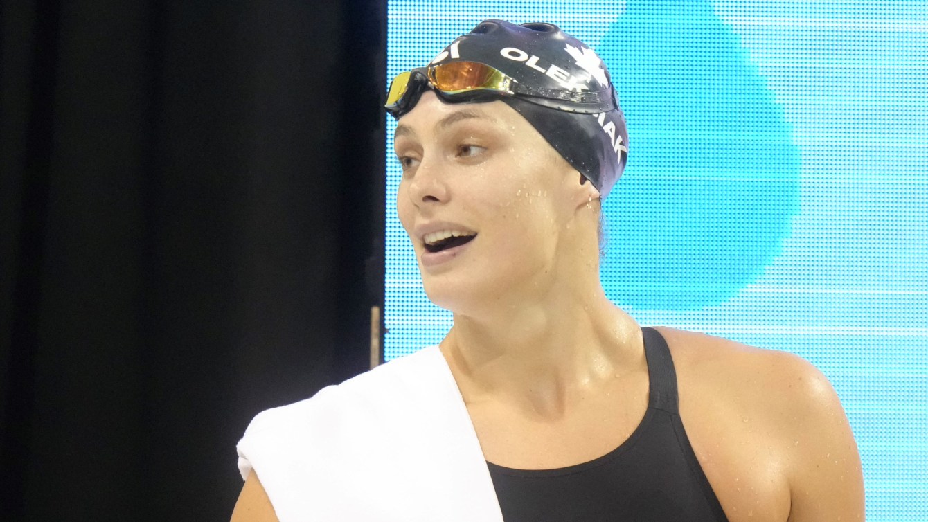 Penny Oleksiak stands on the pool desk with a towel draped over the shoulder 