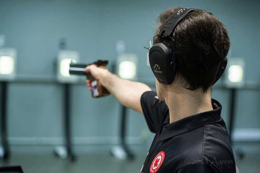 Michele Esercitato competes in the 10m air pistol while wearing large headphones.