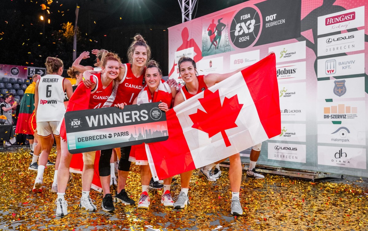 Four Canadian women basketball players hold up a Canadian flag and a big board that says qualified 