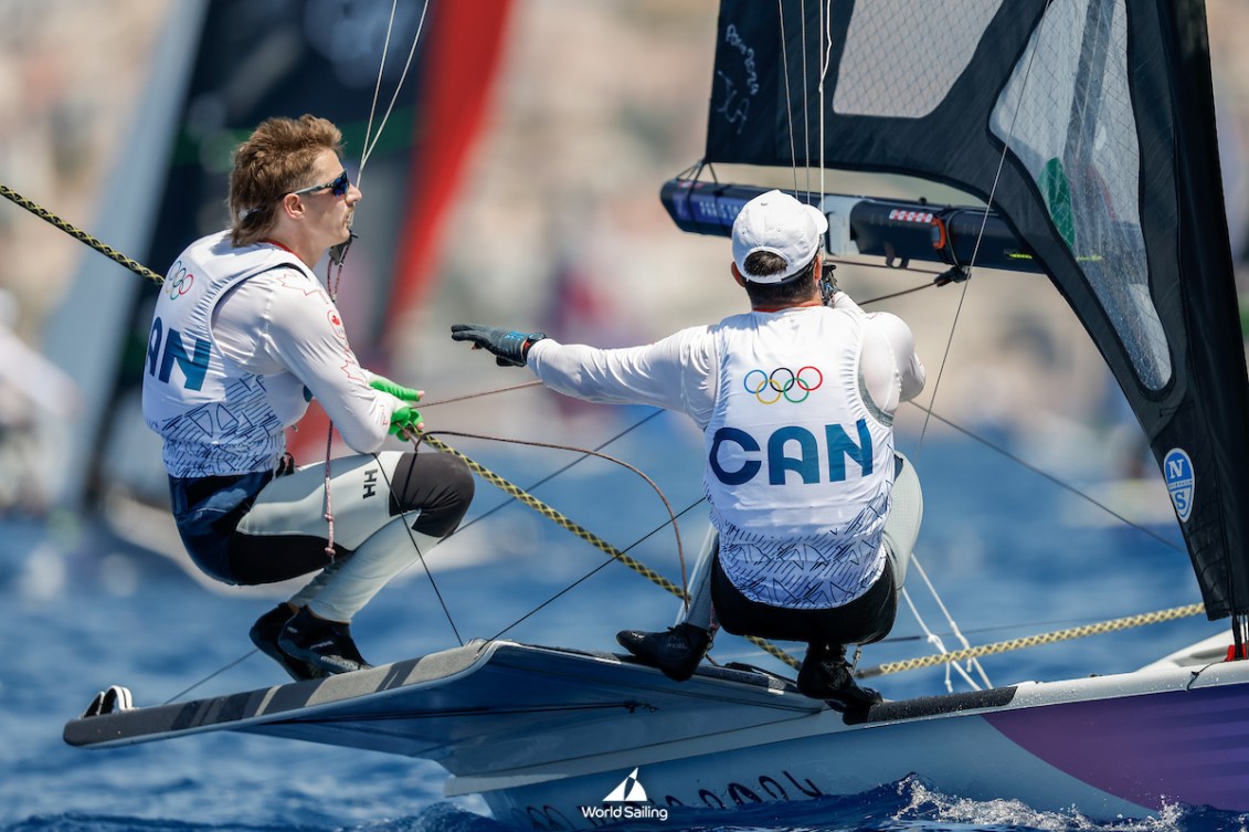 Two sailors in white jackets with their back to camera on their boat 