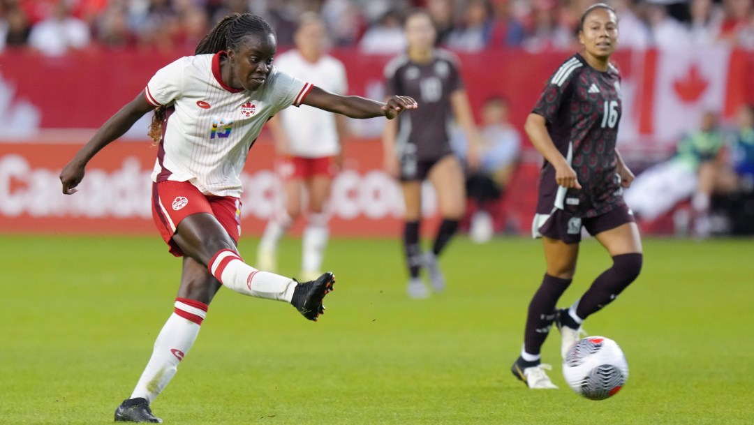 Simi Awujo in a white jersey and red shorts kicks a soccer ball