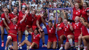 The canadian women's rugby sevens team celebrates in front of a bell they rung after a win