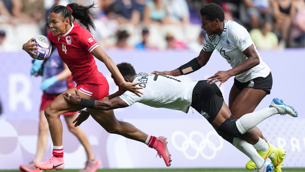 A rugby player in a red jersey outruns a tackle while holding the ball