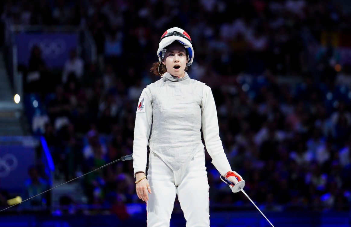 Eleanor Harvey stands in disbelief with her helmet raised after winning a fencing bout