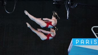 Two divers reach towards their toes in mid-air